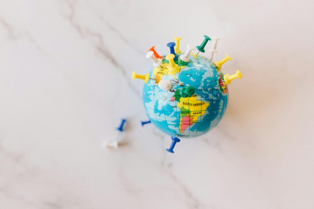 A globe decorated with colorful push pins on a marble surface represents global connections